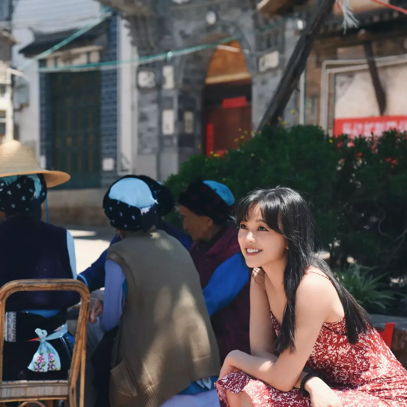 Cristina sitting with older women in blue headscarves on a street in China